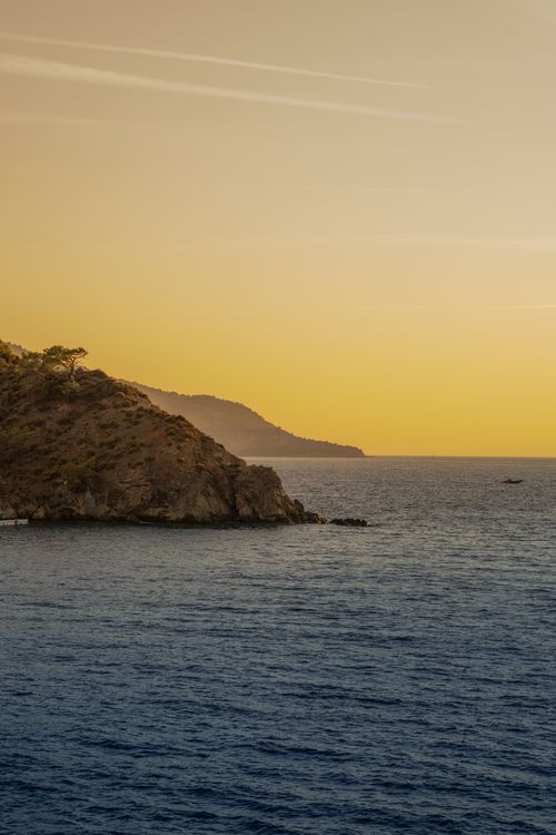 Free Peaceful sunset over a coastal landscape with hills and calm sea. Stock Photo