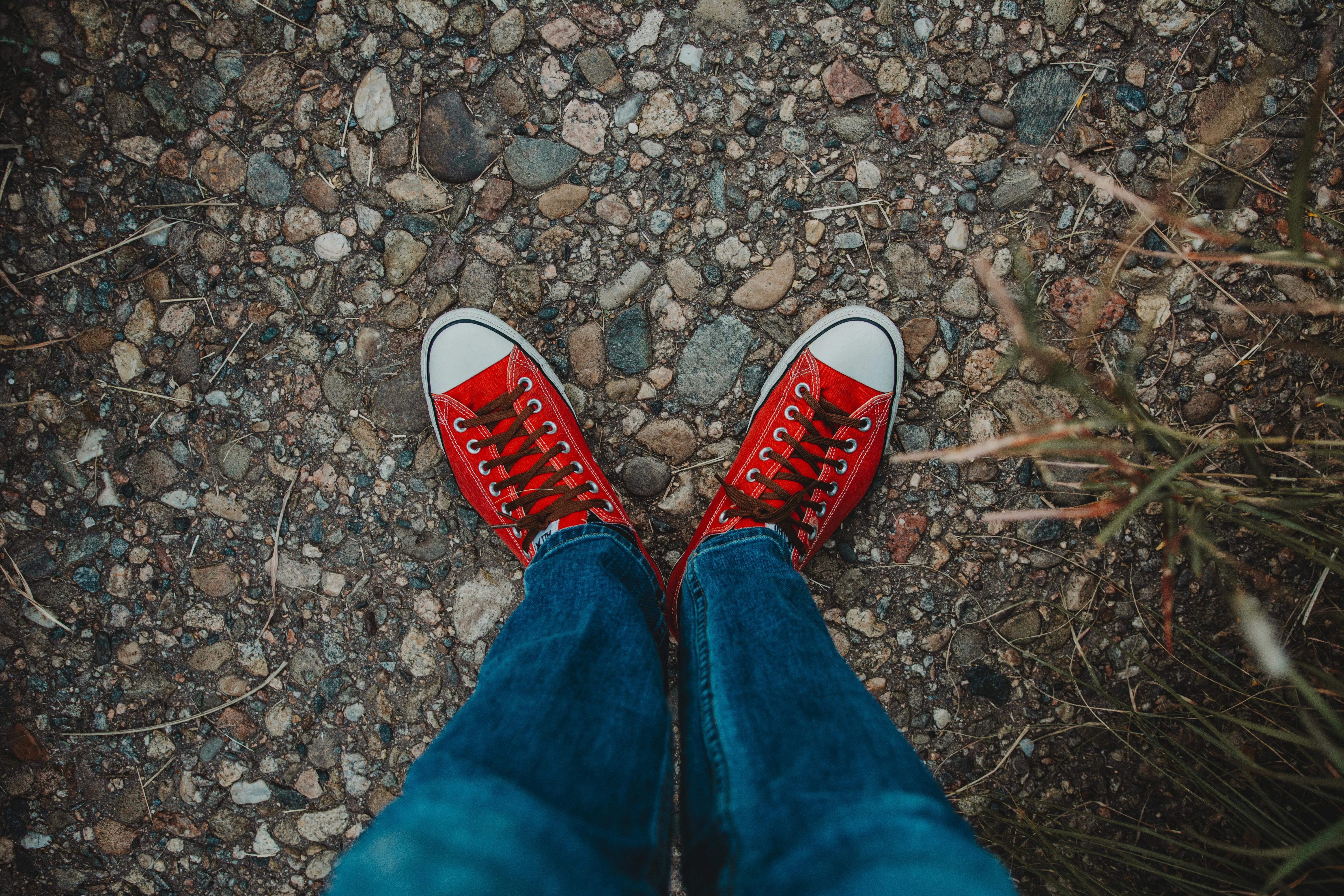A pair of red sneakers standing on a pebbled ground in a casual outdoor setting.