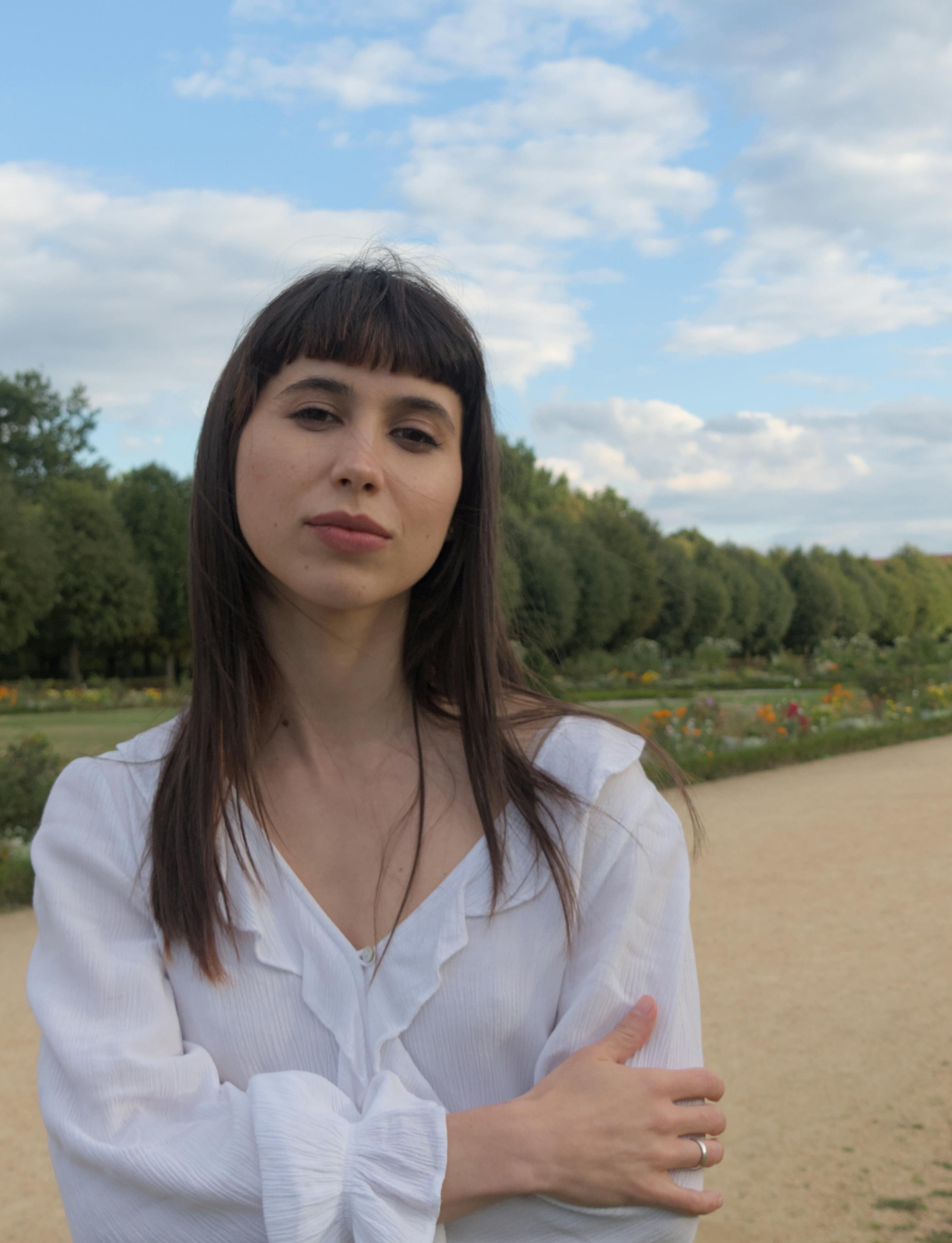 Young woman posing elegantly in a park with greenery and flowers.