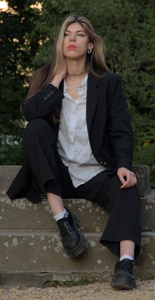 Free Confident young woman in black blazer and blouse sitting outside, exuding fashion-forward style. Stock Photo