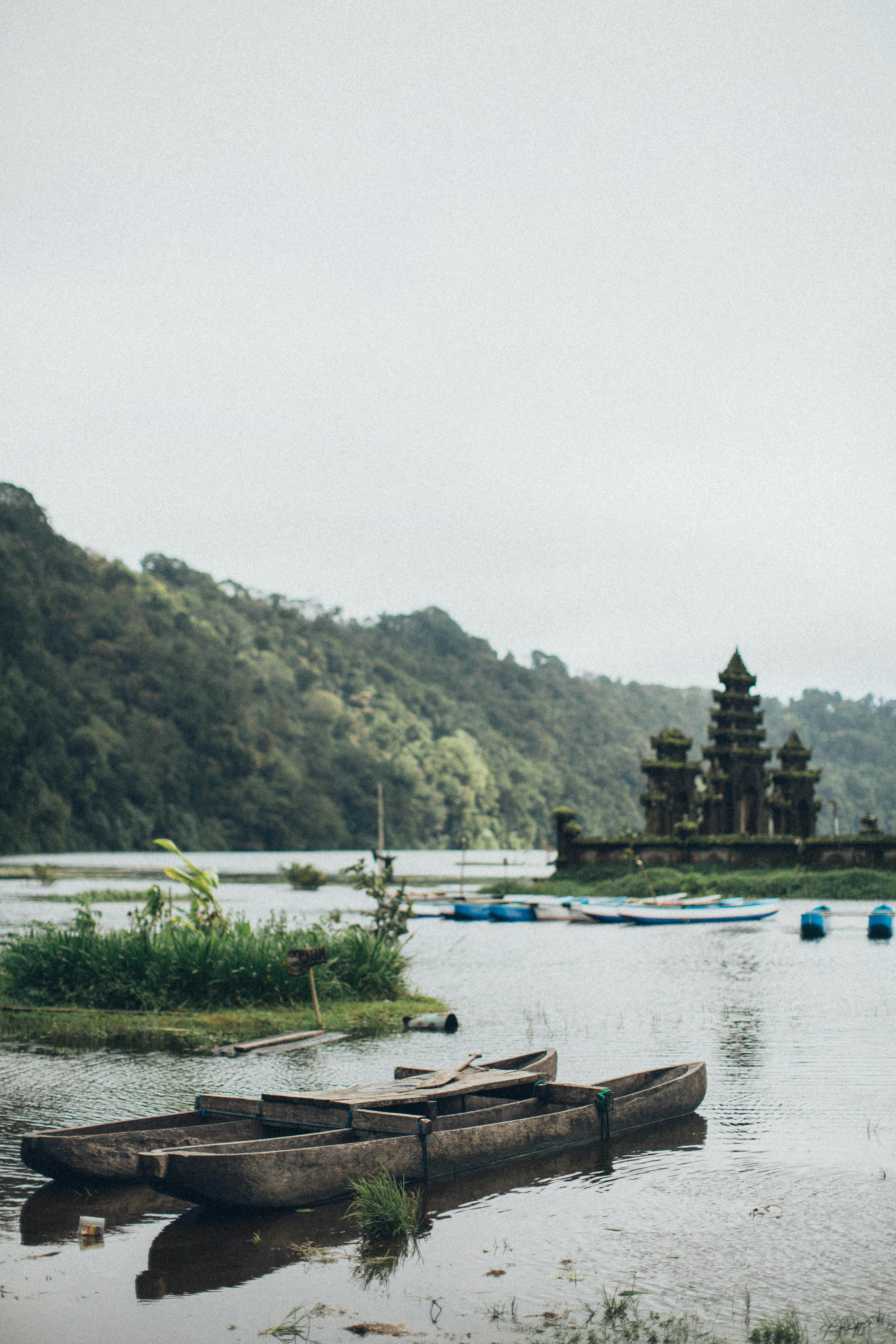 一艘传统的木船停泊在宁静的湖面上，远处是郁郁葱葱的绿意和寺庙，构成了一幅完美的旅行画面
