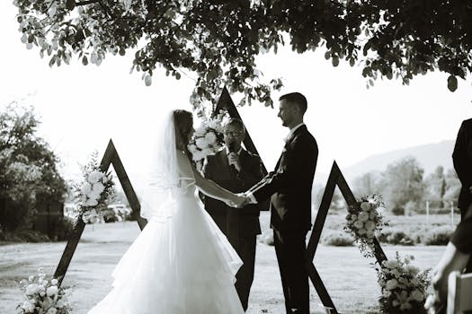 Black and white photo of a couple exchanging vows in an elegant outdoor wedding ceremony.