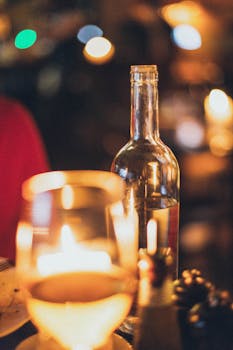 A wine bottle and glass illuminated by candlelight, creating a romantic atmosphere.