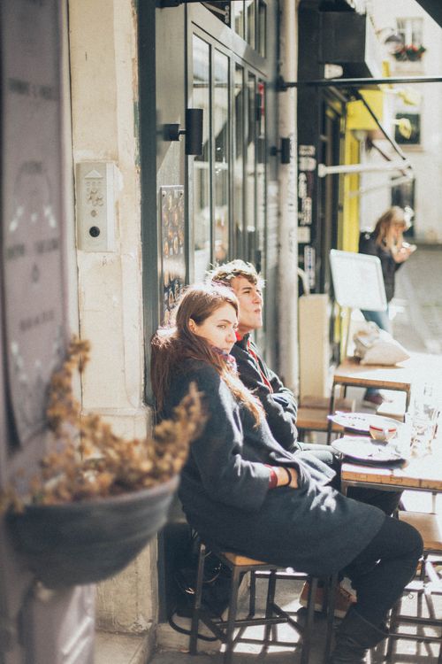 Free A couple enjoys a sunny day sitting at an outdoor café, capturing a moment of relaxation and urban life. Stock Photo