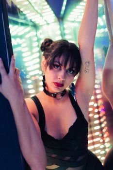 Stylish woman with tattoos poses against a backdrop of colorful, vibrant lights.