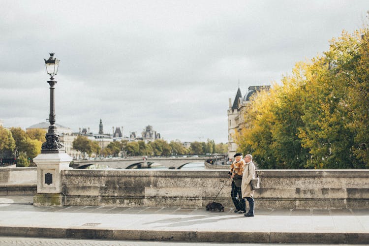 An Elderly Couple Walking On A Bridge With Their Dog 