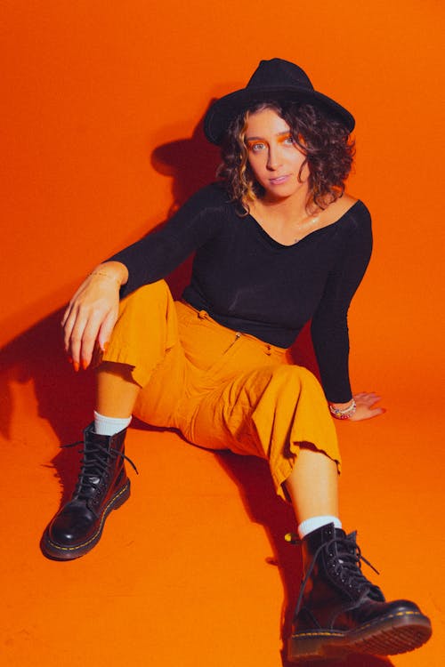 Studio Shot of a Young Woman Wearing a Black Blouse, Hat and Orange Trousers 