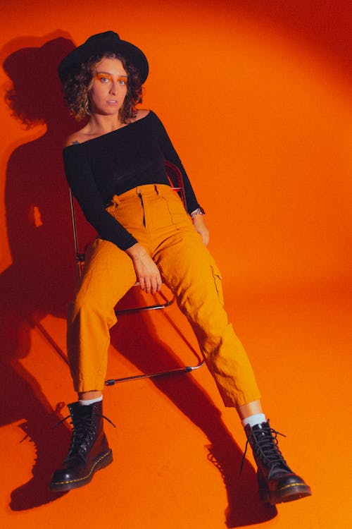 Studio Shot of a Young Woman Wearing a Black Blouse, Hat and Orange Trousers 
