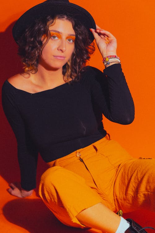 Woman in Hat Sitting on Orange Background