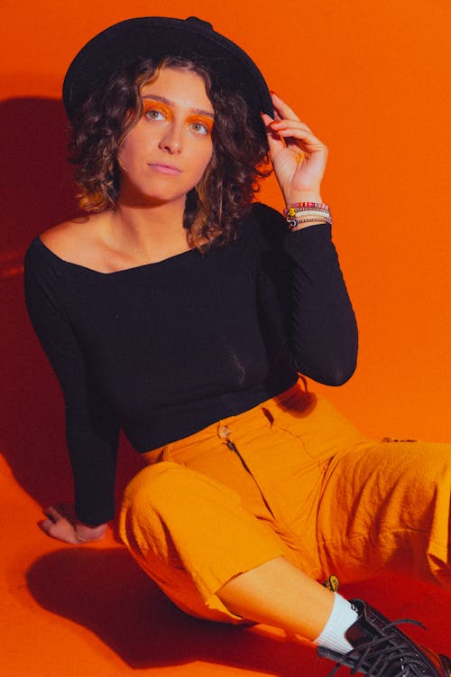 Studio Shot of a Young Woman Wearing a Black Blouse, Hat and Orange Trousers 