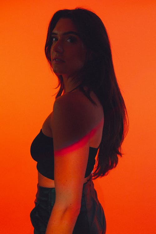 Studio Shot of a Young Brunette in a Casual Outfit Standing against Orange Background 