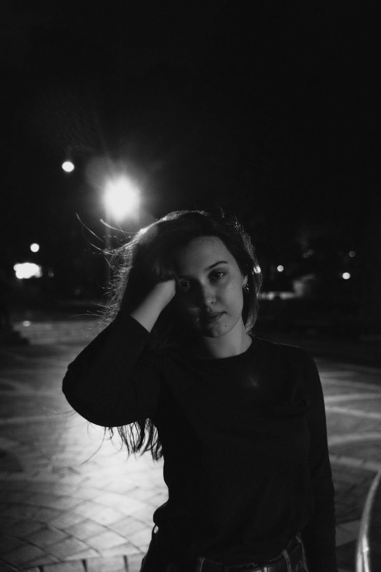 Black And White Photo Of A Young Woman Standing Outside With Hand In Hair 