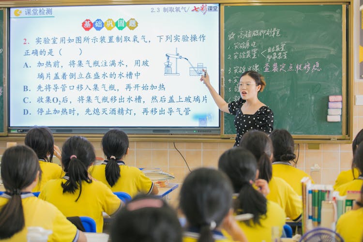 Young Woman Teaching A Group Of School Students At A Chemistry Class