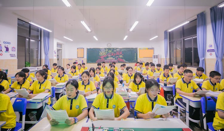 Teenagers In Yellow Polo Shirts Studying At Desks In A Class Room