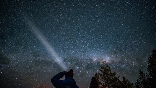Silhouette of a Person with a Flashlight Standing under a Starry Night Sky
