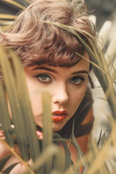 亲密特写中，一位绿眸女子映衬于棕榈叶间，捕捉自然之美