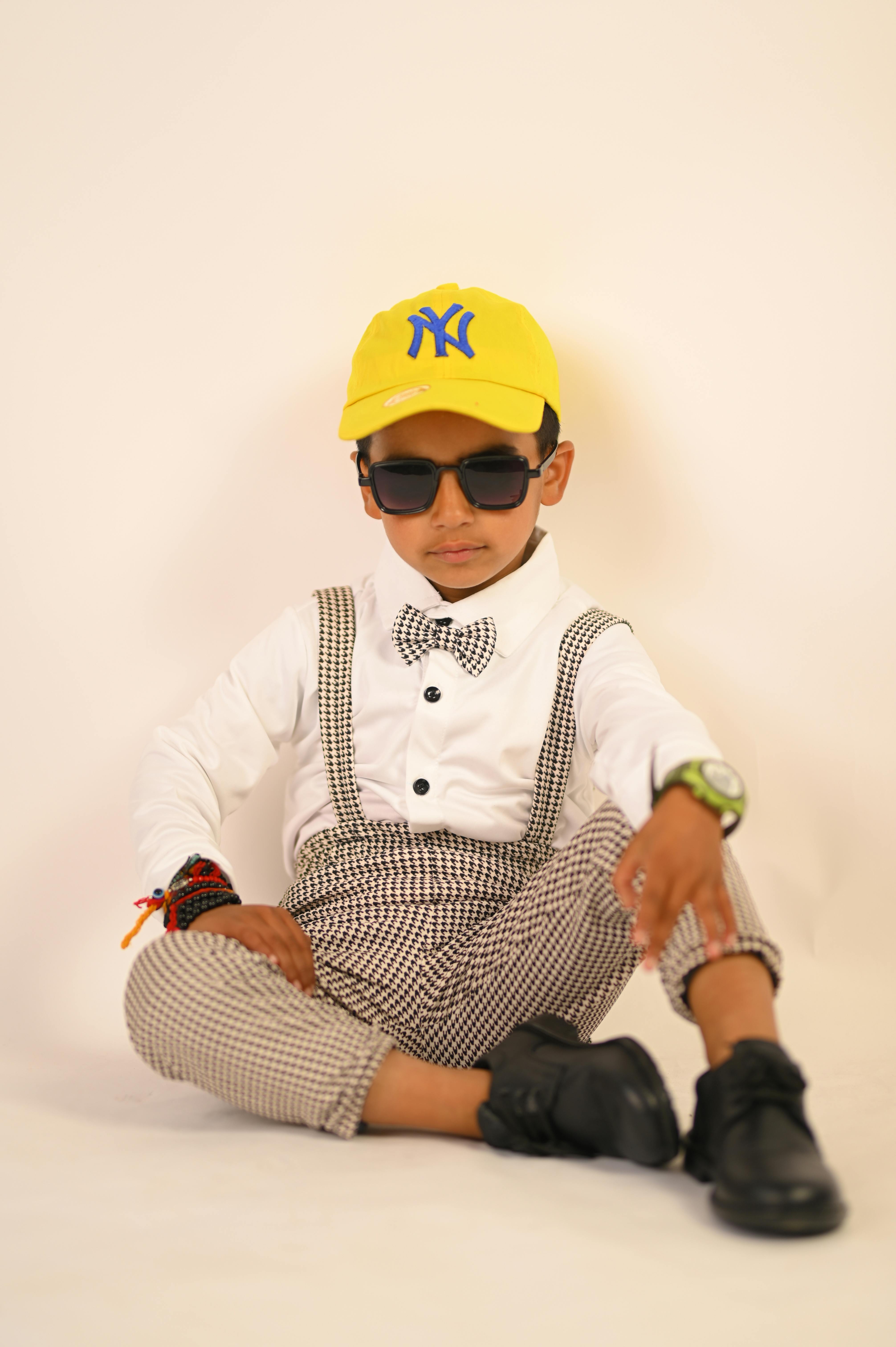 Fashionable young boy posing with sunglasses against a yellow background.