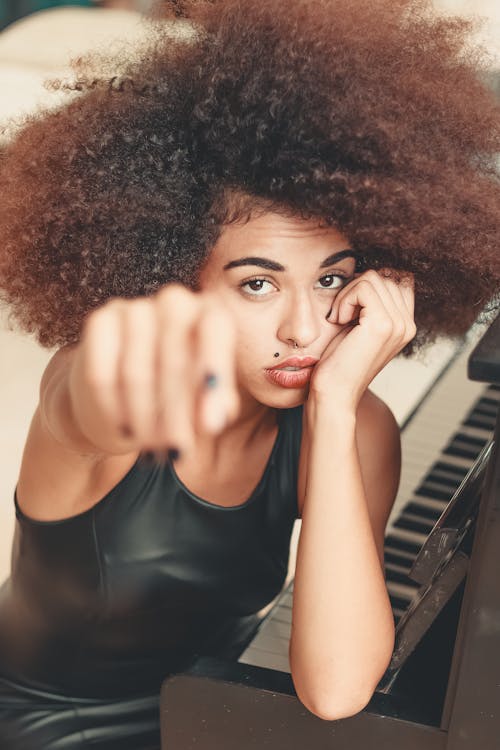 Wanita Bersandar Pada Piano Sambil Mengangkat Tangan Kanan Ke Depan