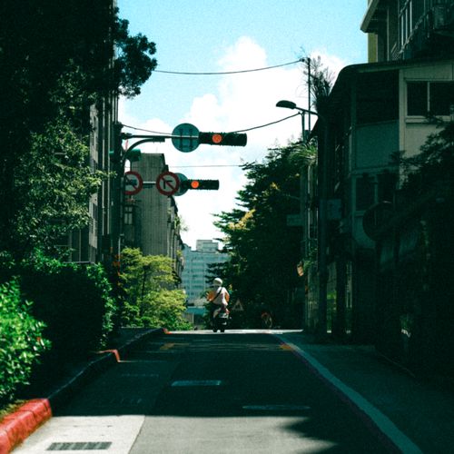 Free A city street with a motor scooter, buildings, and traffic lights under a sunny sky. Stock Photo