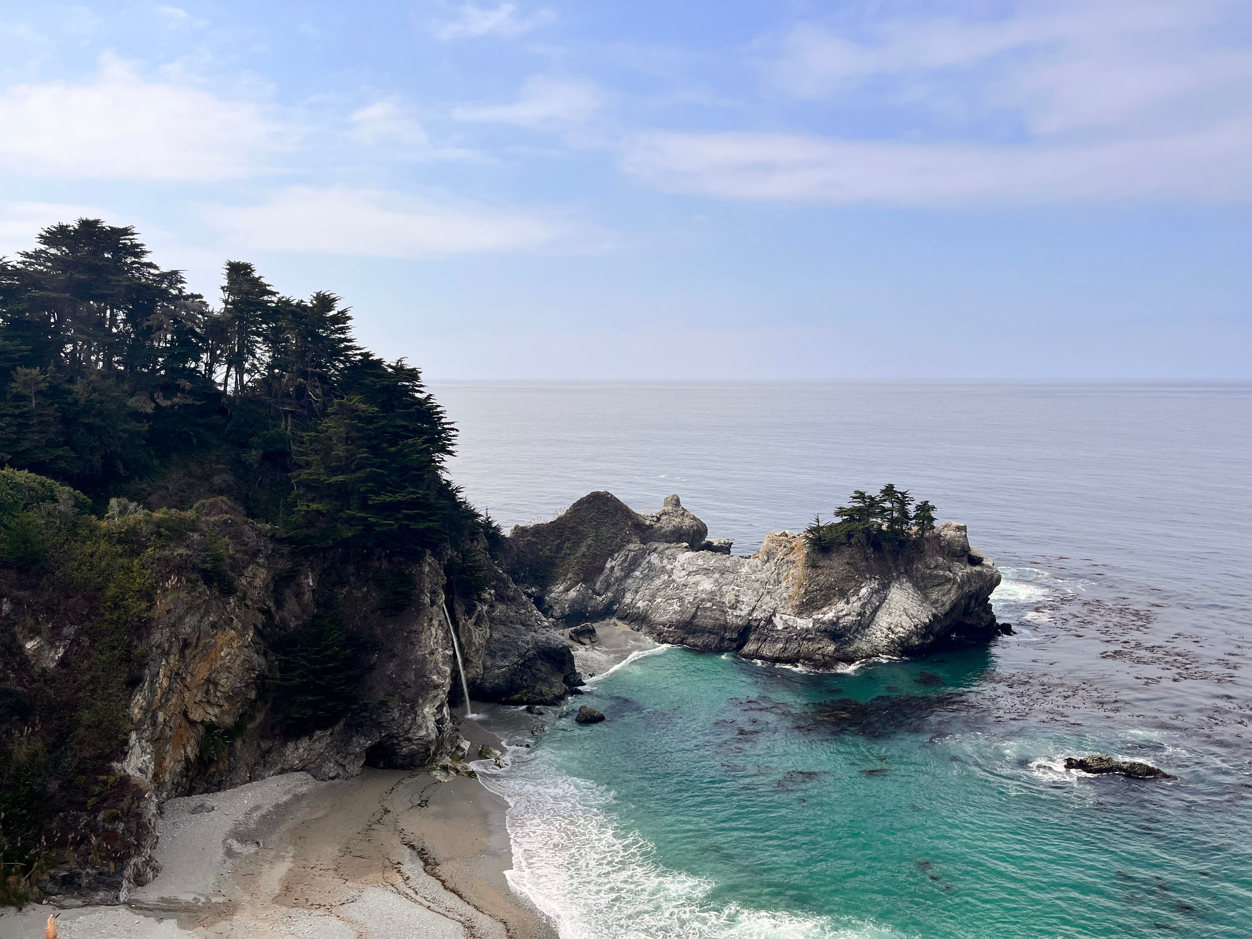 A stunning view of a rocky coastline with clear blue waters and lush trees.