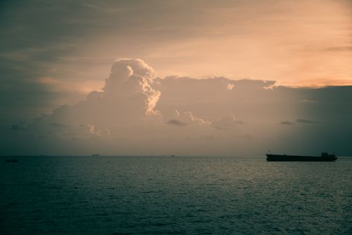 Free A peaceful sunset with a cargo ship on the horizon under dramatic cloud formations at sea. Stock Photo