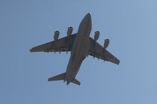Low angle shot of a C-17 Globemaster III, a military transport aircraft flying against a clear blue sky.