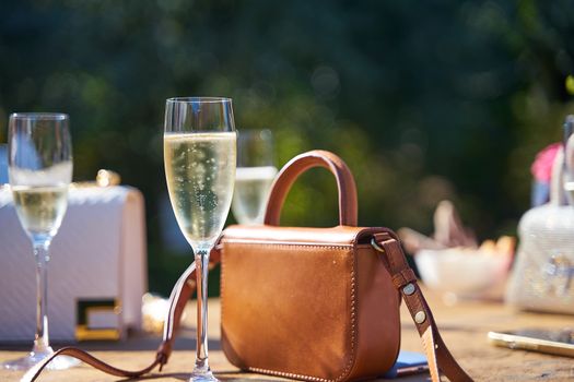 Champagne glasses and a stylish leather bag on a sunlit table, perfect for outdoor celebrations.