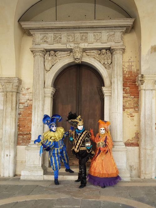 Free Vibrant, costumed figures celebrate Venice Carnival in front of a historic archway. Stock Photo