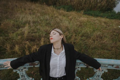 Free Elegant young woman posing outdoors in a field with eyes closed, exuding fashion and grace. Stock Photo