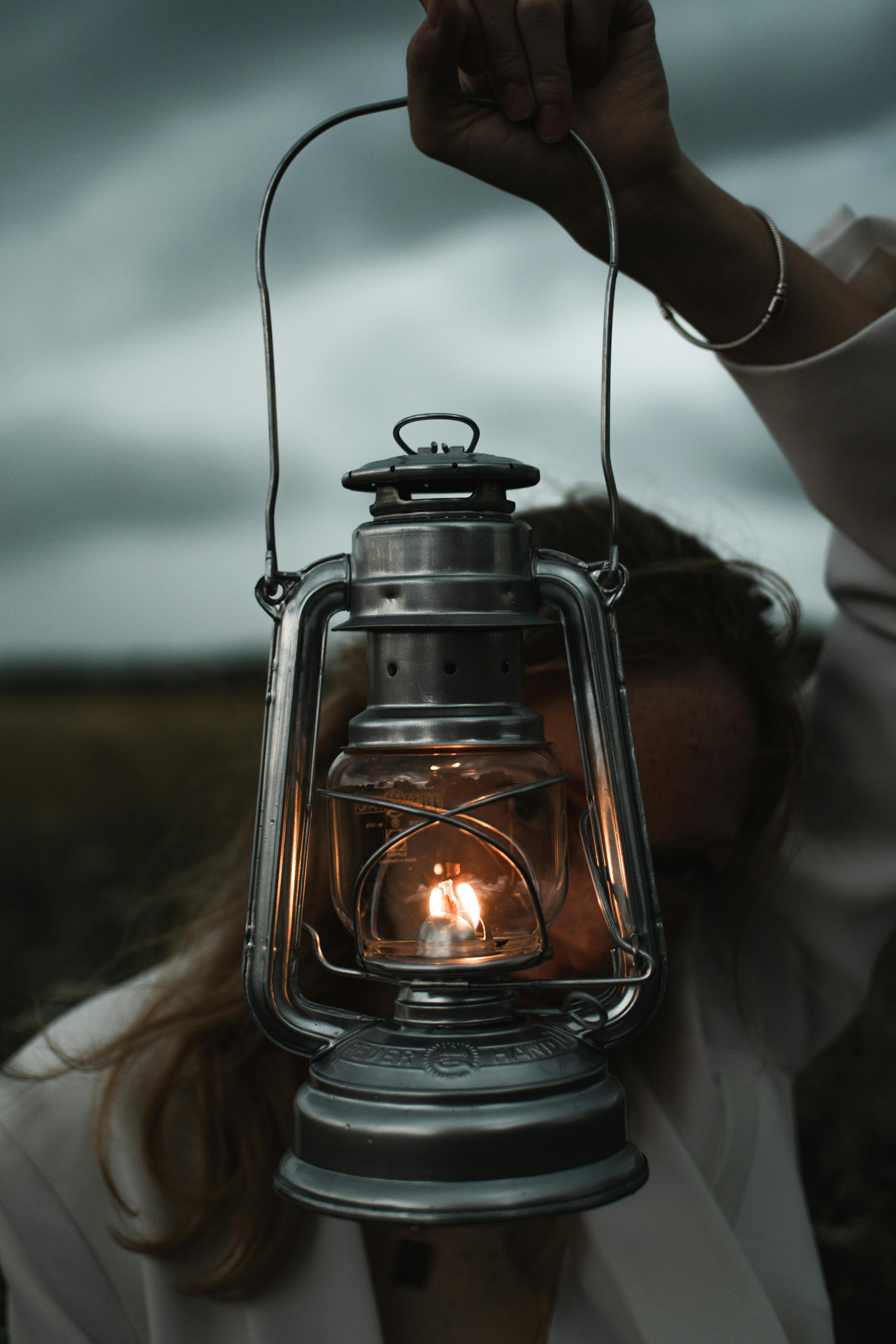 Portrait of a woman holding an illuminated lantern against a moody twilight sky.