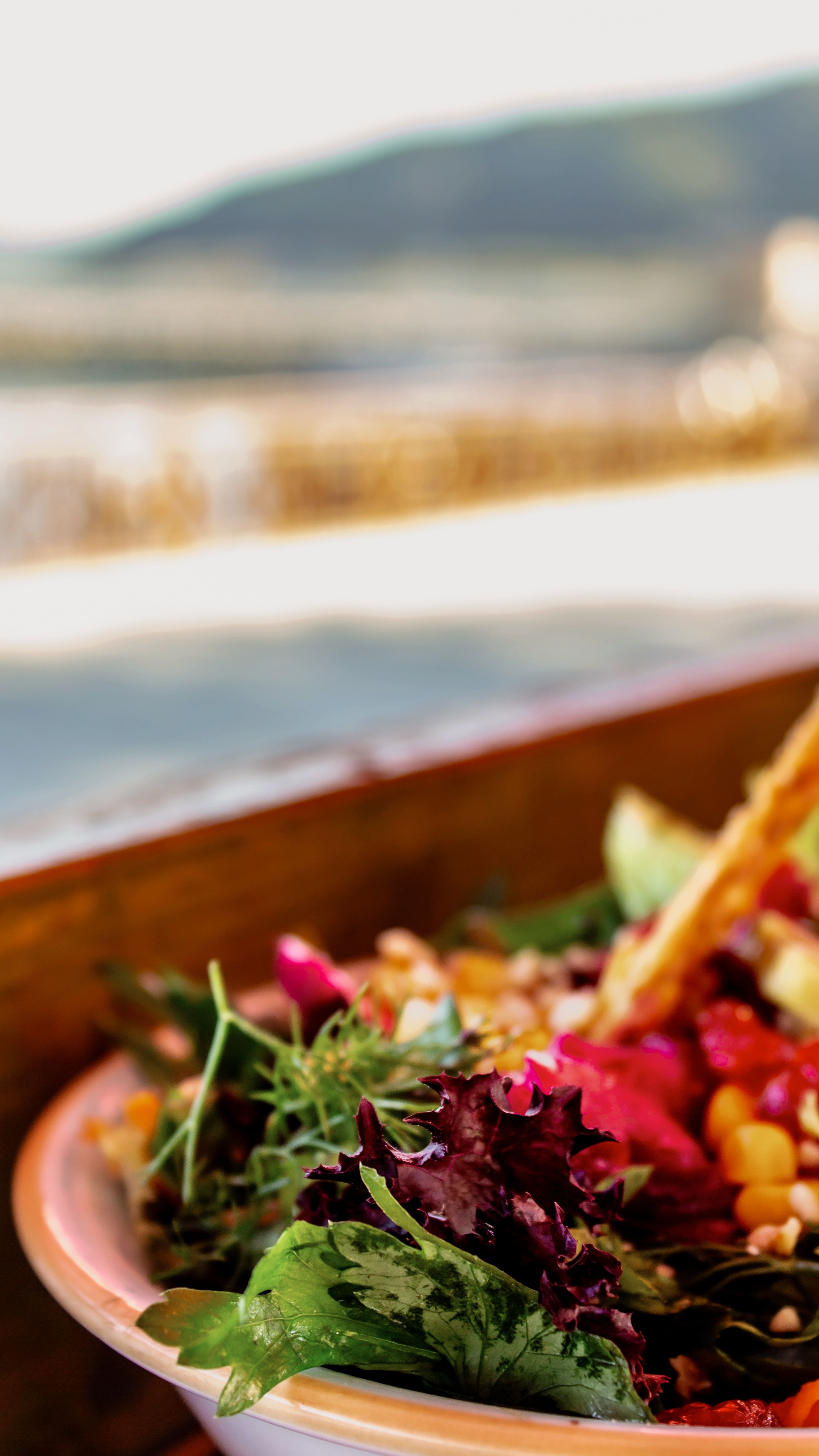 Vibrant fresh salad with leafy greens, captured outdoors with scenic background.