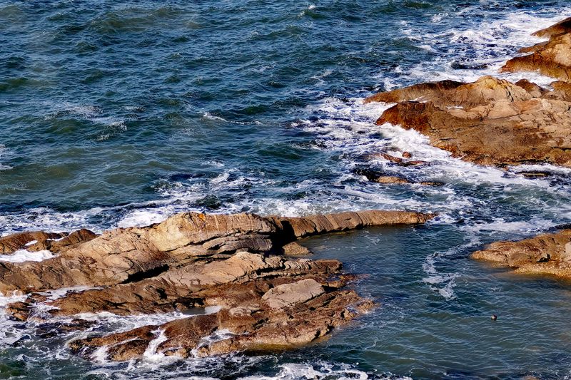 Vibrant image of ocean waves crashing against the rugged rocky shoreline, showcasing nature's raw power and beauty.