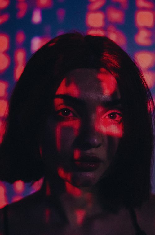 Free Moody portrait of a woman with red and blue light projections on her face, creating an artistic and mysterious ambiance. Stock Photo