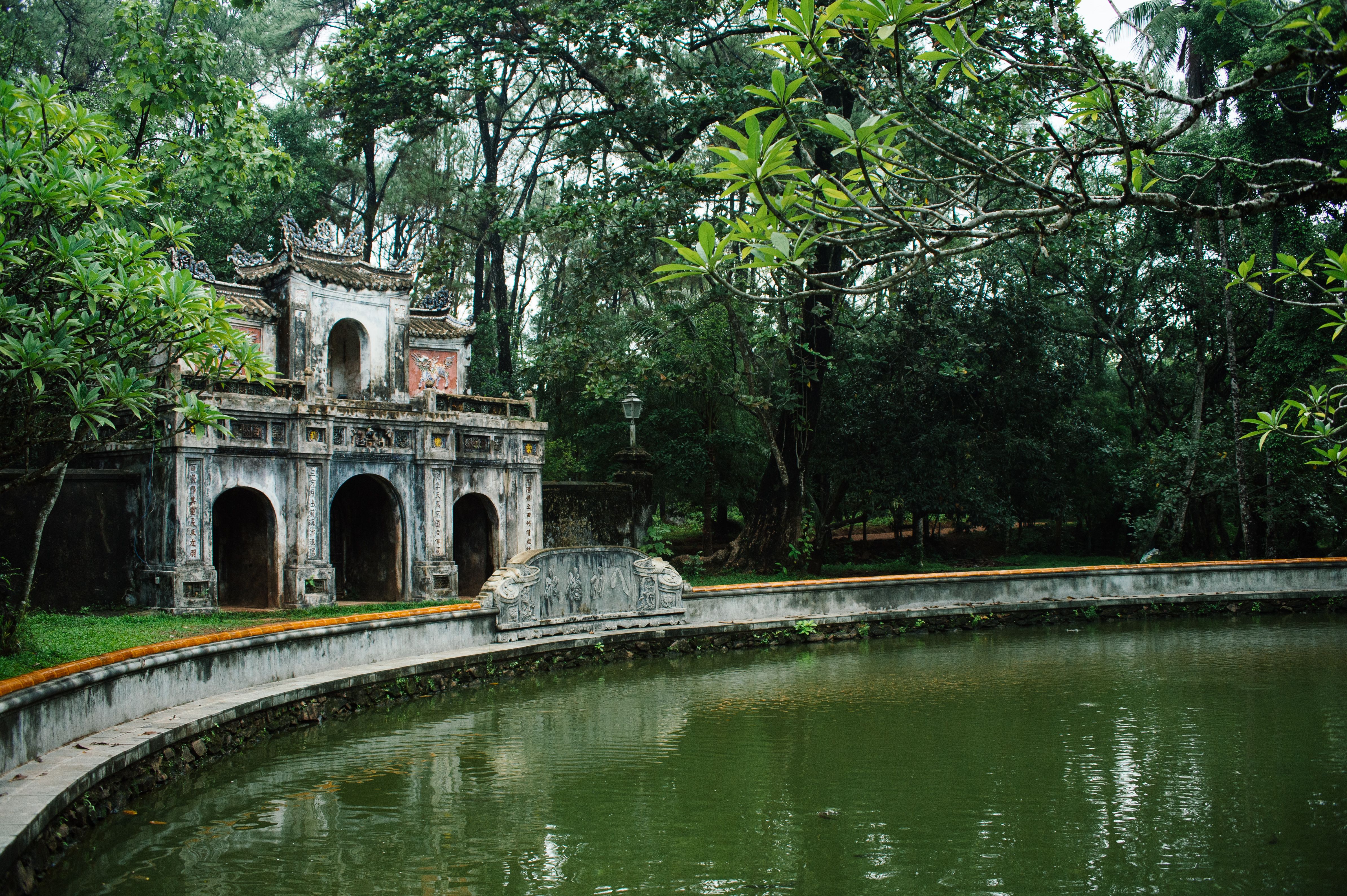 Serene view of Tu Hieu Pagoda by a still pond in Hue, Vietnam, surrounded by lush trees.