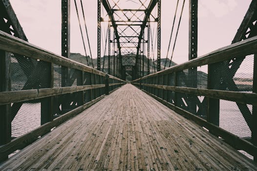 A rustic suspension bridge with wooden flooring spanning across a river, showcasing structural details.