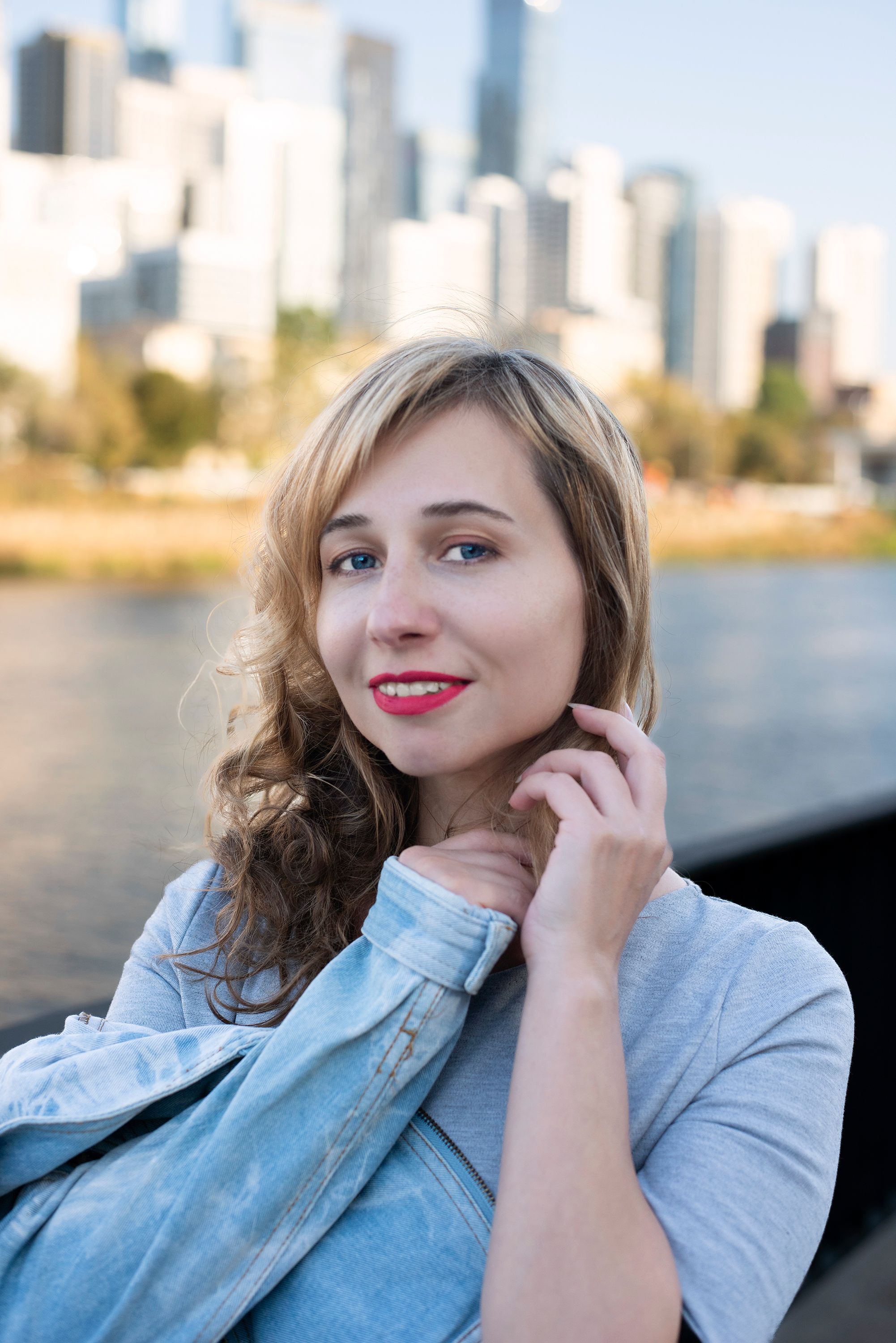 Portrait of a smiling woman with long blonde hair against an urban skyline backdrop.