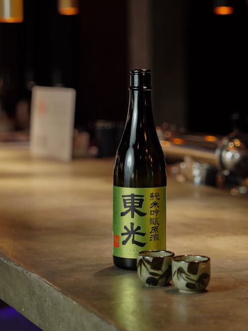 A Drink in a Glass Bottle and Small Cups on the Bar Counter