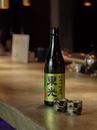 Bottle of Japanese sake with two ceramic cups on a dimly lit bar counter, perfect for tasting.