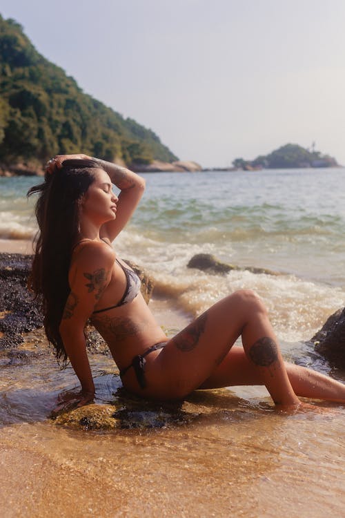 бесплатная Женщина в бикини, сидящая на берегу Стоковое фото