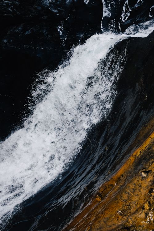Free A powerful waterfall cascading down a steep cliff, splashing over rocks into a dark pool below. Stock Photo