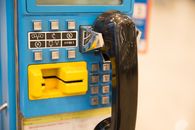 Close-up of a retro blue telephone booth with a black handset and coin slot.