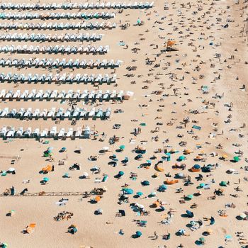 A stunning aerial view of a crowded beach in Nazaré, Portugal with sunbeds and umbrellas.