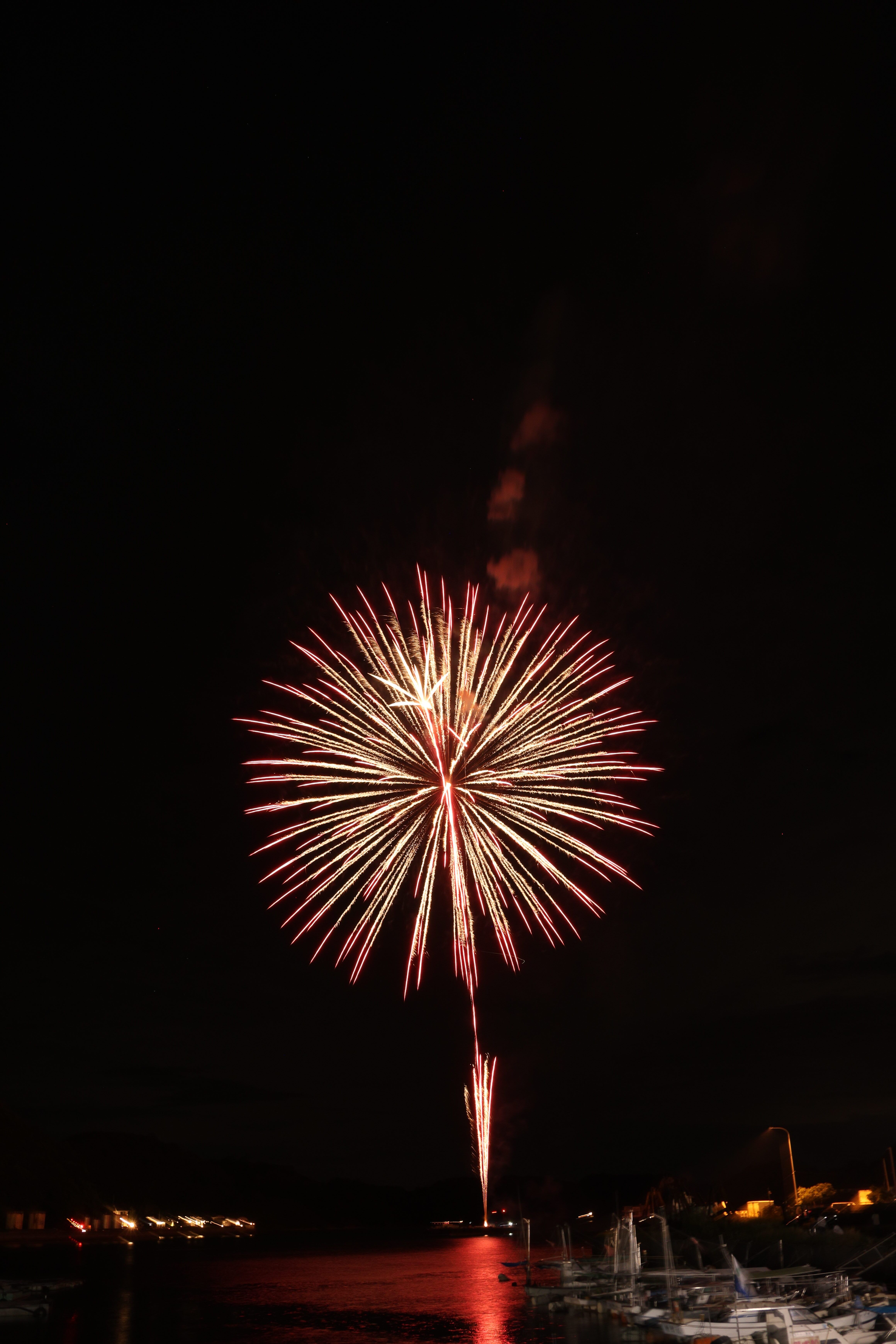 A stunning display of fireworks illuminates the night sky over a marina, reflecting on the water.