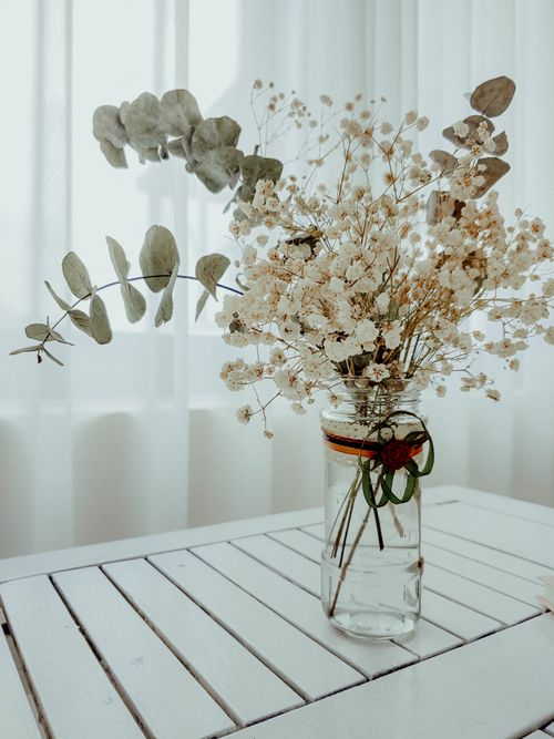 Free A rustic dried flower arrangement in a glass vase on a white table by a curtain, perfect for minimalist decor. Stock Photo