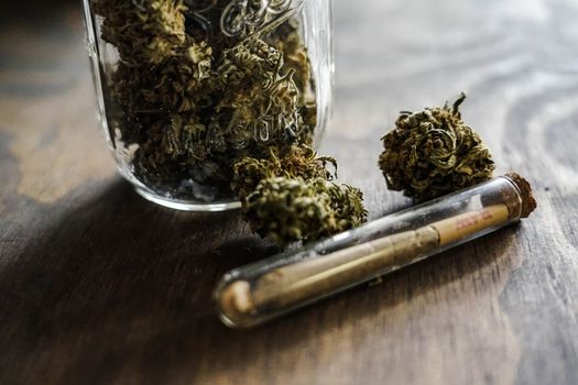 A detailed close-up of cannabis buds in a jar with a joint on a wooden surface.