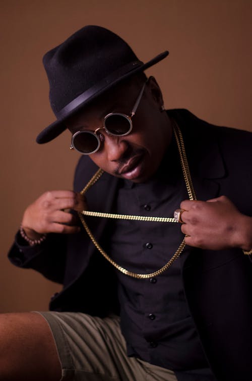 Man in Black Blazer and Brown Short Pulling His Gold Necklace With Both Hands