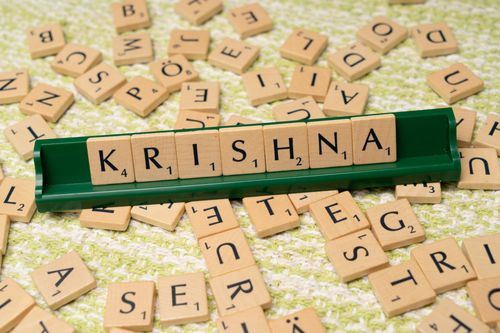 Free Wooden Scrabble tiles spelling 'Krishna' on a green rack amidst scattered tiles. Stock Photo