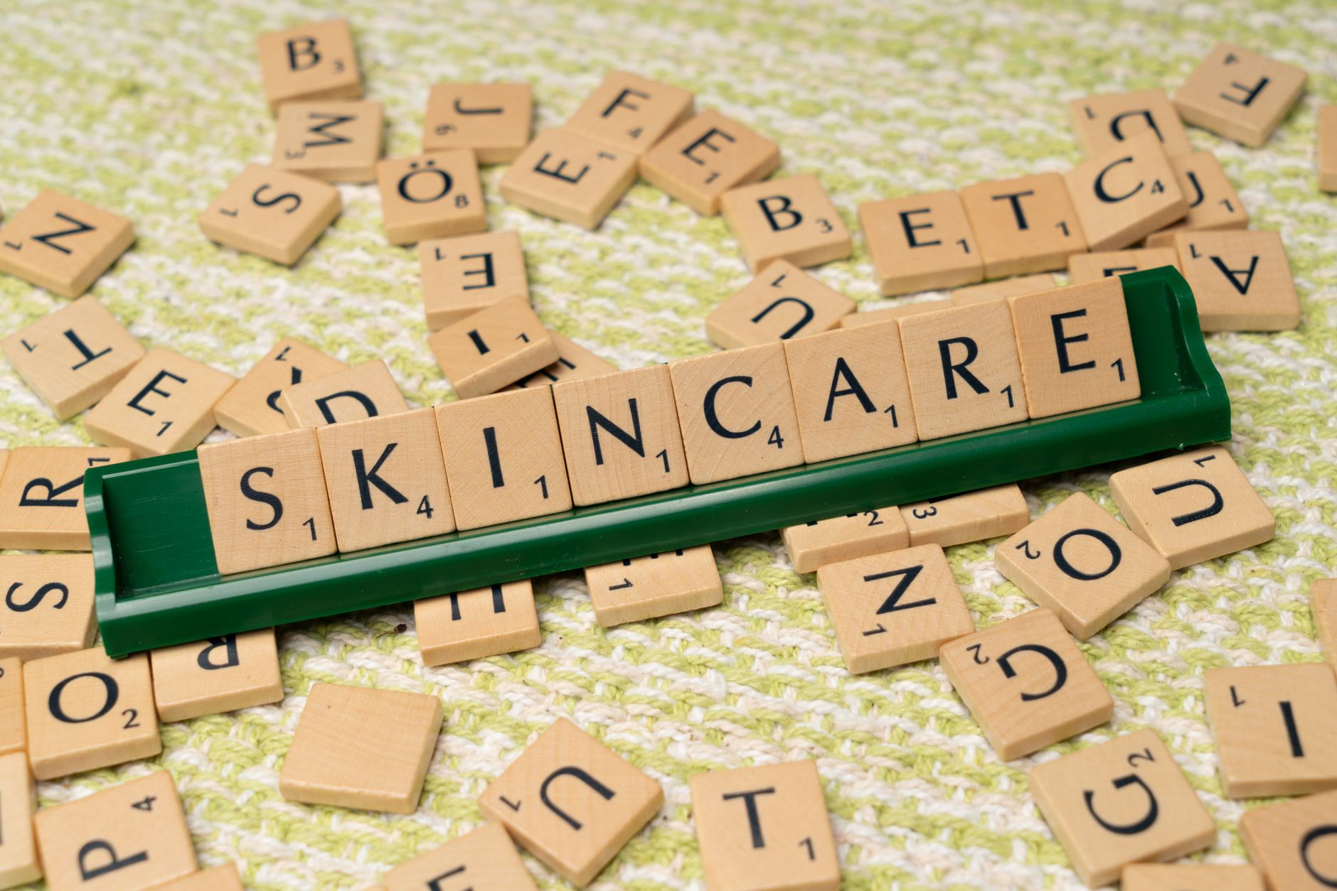 Scrabble tiles spelling 'skincare' on a green textured surface, representing beauty and wellness.