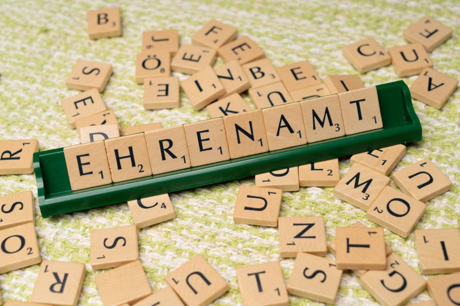 緑のタイルホルダーの上に散らばったタイルとともに'Ehrenamt'を綴る木製の文字タイルのクローズアップ。