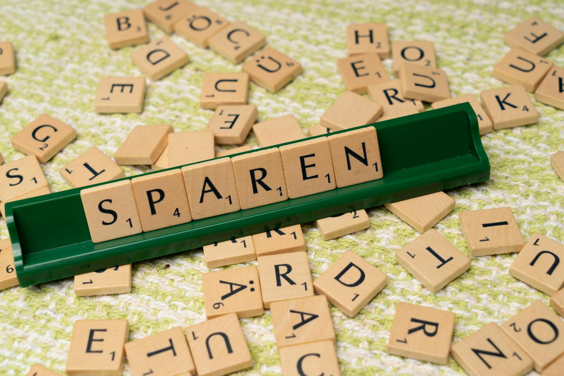 Close-up of Scrabble tiles spelling 'Sparen' on a green tile holder.